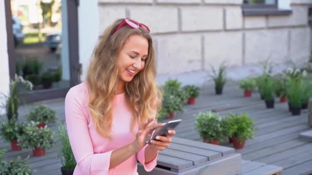 Destul de tânără femeie mesaje text prin telefon. O femeie fericită în cafeneaua în aer liber — Videoclip de stoc