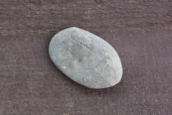 Μια επίπεδη πέτρα που βρίσκεται σε μια ξύλινη επιφάνεια. — Φωτογραφία Αρχείου