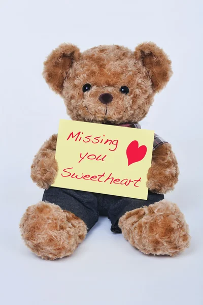 A cute teddy bear holding a yellow sign that says Missing my sweetheart isolated on a white background — Stock Photo, Image