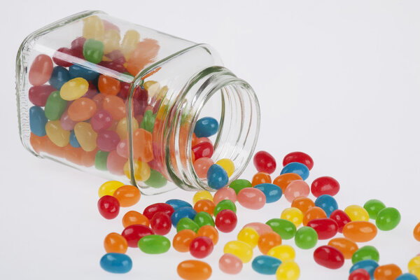 Close up of a delicious Jelly Beans candy spilled from a glass jar isolated on a white background