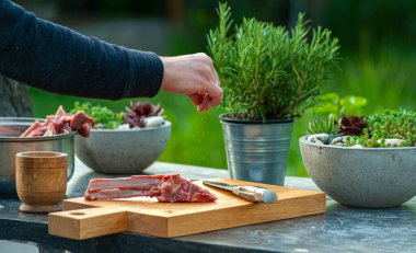 Kuzu pirzolasına baharat katan bir adam ahşap kesme tahtasında, açık havada 