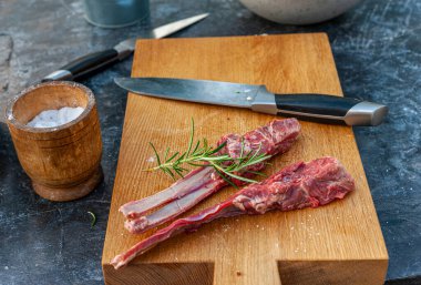 Biberiyeli, baharatlı kuzu pirzolaları ve siyah taş masanın üzerindeki tahta kesme tahtasının üzerinde büyük bir bıçak.