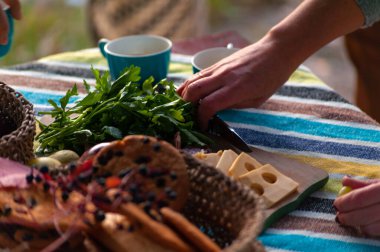 Hasır sepetlerde kurabiyeler dilimlenmiş peynir, sosis ve bir sürü yeşillik olan bir masa.