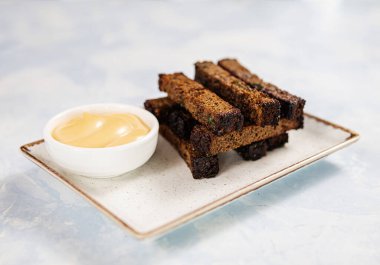 Mavi arka planda dikdörtgen bir tabakta peynir soslu kızarmış ekmek. 