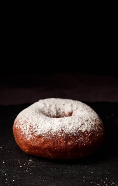 Siyah zemin üzerine pudra şekeri serpiştirilmiş çörek.