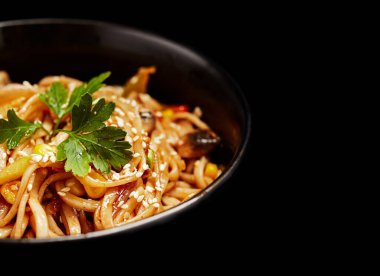 Sebzeli erişte ve siyah arka planda bir tabakta susam tohumu.