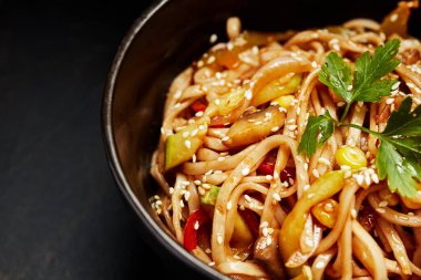 Sebzeli erişte ve siyah arka planda bir tabakta susam tohumu.