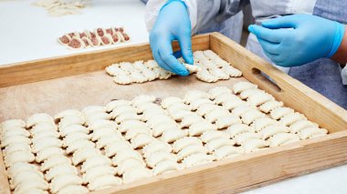 Mavi eldivenli işçi ahşap tepsiye hamur tatlısı koyar.