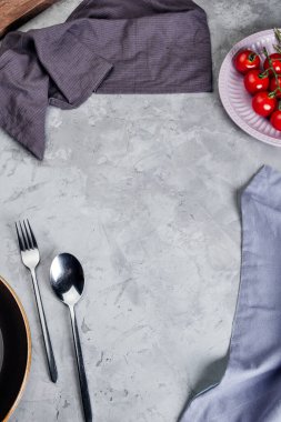 Çatal bıçak, peçete ve kiraz domatesli gri dokuma.