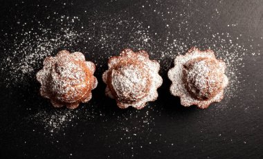 Siyah arkaplan manzarasına pudra şekeri serpiştirilmiş kekler.