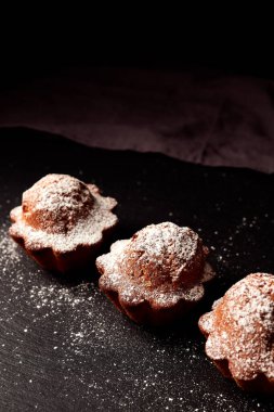 Siyah arkaplana pudra şekeri serpiştirilmiş kekler.