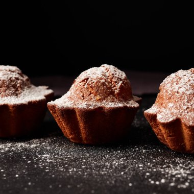 Siyah arkaplana pudra şekeri serpiştirilmiş kekler.