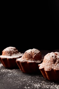 Siyah arkaplana pudra şekeri serpiştirilmiş kekler.