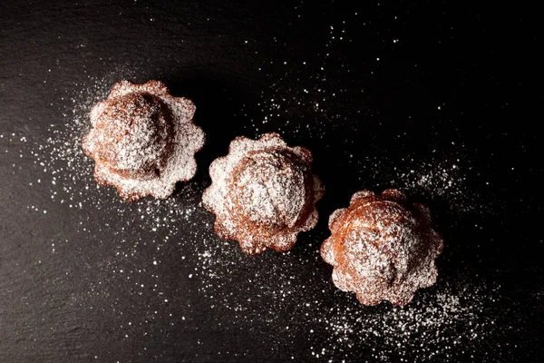 Siyah arkaplan manzarasına pudra şekeri serpiştirilmiş kekler.