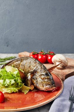 Turuncu tabakta marul ve domatesli ızgara balık.