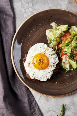 Çırpılmış yumurta ve salata kahverengi bir tabakta, üzerinde domates ve mantar olan ahşap bir tahtanın yanında gri beton arka plan manzaralı.
