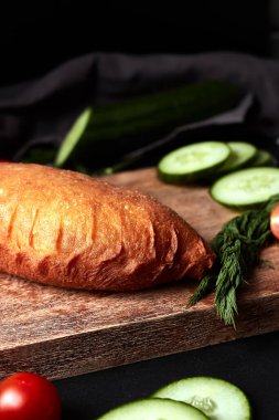 Tahtada salatalıklı, otlu, domatesli ve siyah arka planda peçeteli bir Patty. 