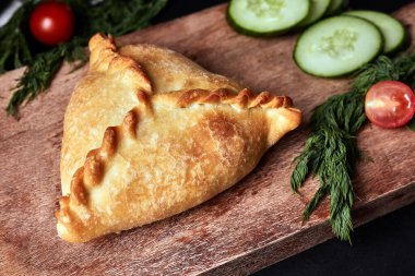 Tahtada üç köşeli turta ve siyah arka planda salatalıklı domates. 