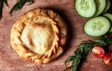 Tahtada yuvarlak bir turta, salatalıklı, domatesli, otlu.