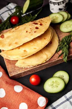 Ahşap zemin üzerinde patates püresiyle kızarmış tortilla salatalık domates otları ve siyah arka planda kahve.