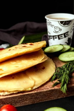 Ahşap zemin üzerinde patates püresiyle kızarmış tortilla salatalık domates otları ve siyah arka planda kahve.