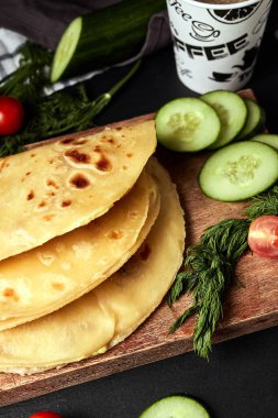 Ahşap zemin üzerinde patates püresiyle kızarmış tortilla salatalık domates otları ve siyah arka planda kahve.