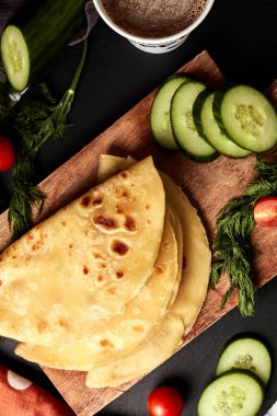 Ahşap zemin üzerinde patates püresiyle kızarmış tortilla salatalık domates otları ve siyah arka plan manzaralı kahve.