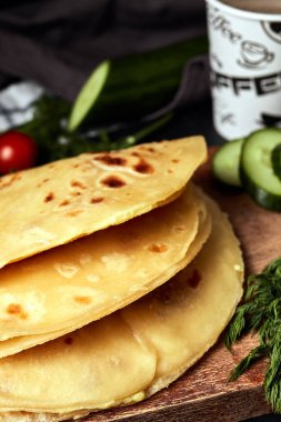 Ahşap zemin üzerinde patates püresiyle kızarmış tortilla salatalık domates otları ve siyah arka planda kahve. 