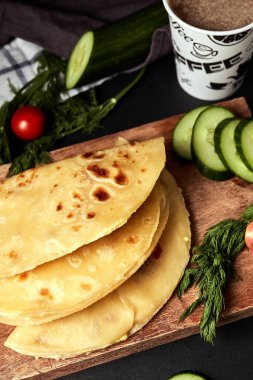 Ahşap zemin üzerinde patates püresiyle kızarmış tortilla salatalık domates otları ve siyah arka planda kahve. 