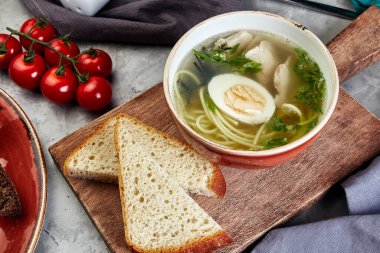 Tahtada yumurta ve spagetti ile tavuk çorbası. Ekmek ve gri beton arka planda domatesler.