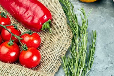 Çuval bezinde domates ve kırmızı biber, gri çimento arka planda bitkiler.