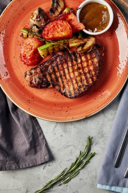 Izgarada pişmiş pirzola, gri beton arka plan manzaralı soslu bir tabakta sebzelerle.