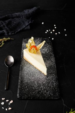 Siyah arka planda siyah tahta üzerine pudra şekeri serpiştirilmiş cheesecake.