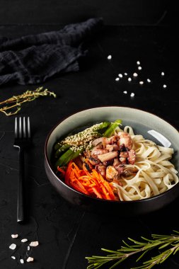 Siyah desenli bir tabakta et ve sebzeli Çin eriştesi.