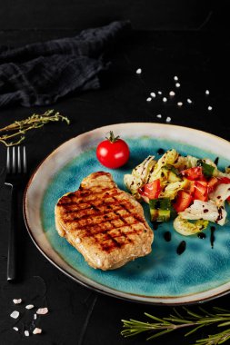 Siyah desenli arka planda kahverengi tabakta sebzeli ızgara et.