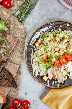 Çuval bezi ve domatesli gri beton arka planda sezar salatası.