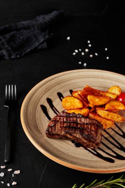 Siyah desenli arka planda kahverengi bir tabakta soslu kızarmış patates.