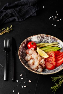 Sebzeli soyulmuş karides, siyah desenli arka planda bir tabakta.