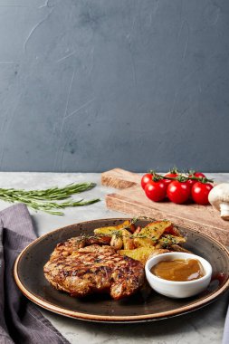 Kır patatesli ızgara biftek ve gri bir arka planda kahverengi bir tabakta sos.
