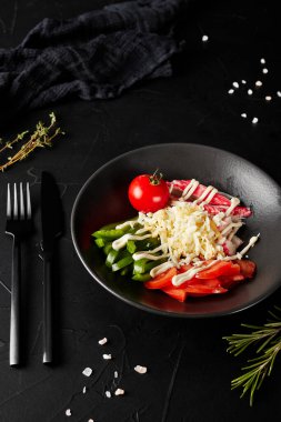 Siyah bir tabakta kesilmiş sebzeler ve koyu dokulu bir arka plan.