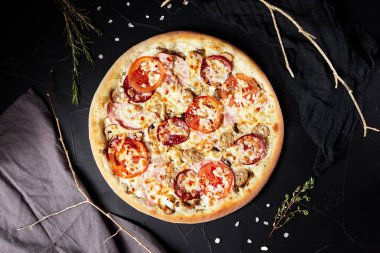 pizza siyah desenli arka planda koyu peçete ve altın dallar üst manzaralı