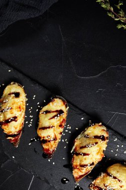 Kara tahtada pişmiş istiridye. Koyu bir arka planda. Üstü altın renkli bir filizle.