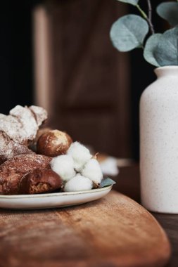Tahtada ekmek ve pamuklu bir tabak vazoda dekoratif bir çiçeğin yanında.