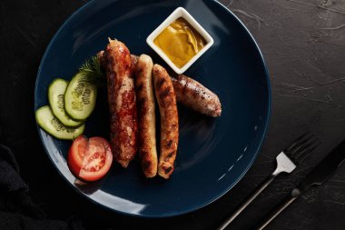 Siyah arka planda mavi tabakta sebzeli ızgara sosis.