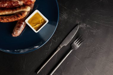 Siyah arka planda mavi tabakta sebzeli ızgara sosis.