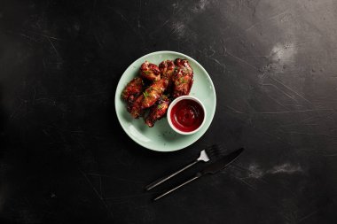 Arka planda siyah desenli bir manzarada açık tabakta ketçaplı tavuk kanatları