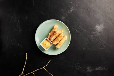 Peynir, siyah desenli arka planda açık bir tabakta, altın bir çalı çırpı görünümlü.