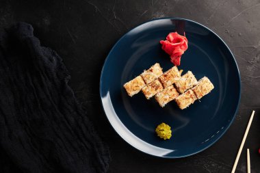 Siyah desenli arka planda mavi bir tabakta ton balığı parçacıklı rulo.