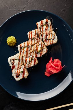 Siyah desenli arka planda mavi bir tabakta yılan balığıyla yuvarlanıyor.