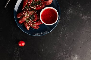 Siyah arka planda mavi tabakta sebzeli ızgara sosis.